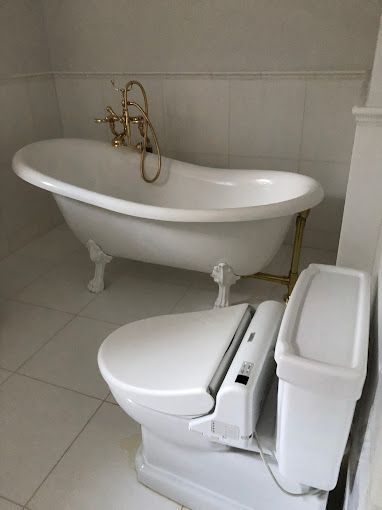 White clawfoot bathtub and modern toilet with bidet seat in a bathroom. Gold fixtures.