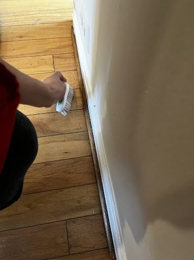 Person cleaning hardwood floor near a wall with a brush.
