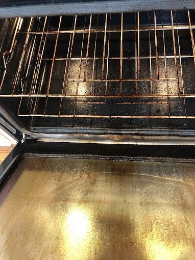 Inside of a dirty oven with a rack and a bottom tray covered in stains.