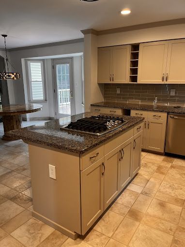 Kitchen with beige cabinets, granite countertops, and an island with a stovetop. Light-colored tile floor.