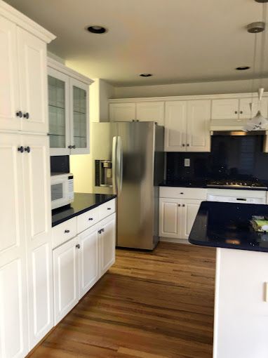 White kitchen with stainless steel refrigerator, dark countertops, and wood floors.