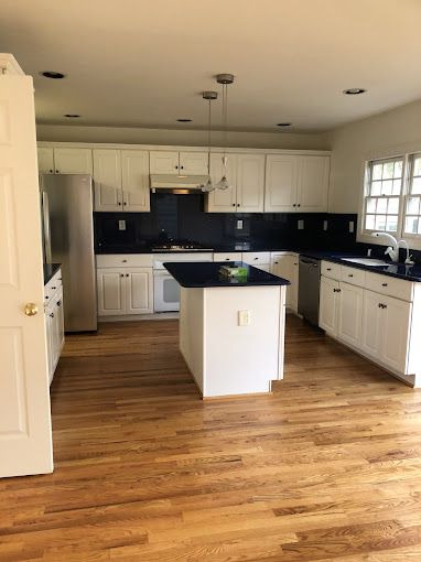 White kitchen with dark backsplash and island, wood floor.