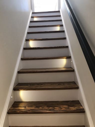 Wooden staircase with built-in lights on each step, leading upwards to a bright opening.