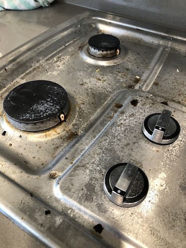 Dirty gas stovetop with three burners and control knobs.
