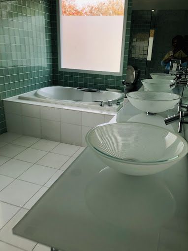 Modern bathroom with jacuzzi tub and glass sinks, light green tile, white countertops, and frosted window.