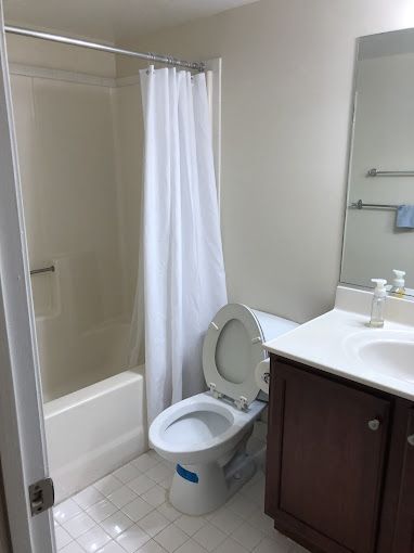 Bathroom with a toilet, shower/tub, vanity, and a partially open door. White, cream, and brown tones.