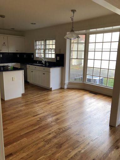 Kitchen with white cabinets, dark countertops, and wood flooring. Bay window.