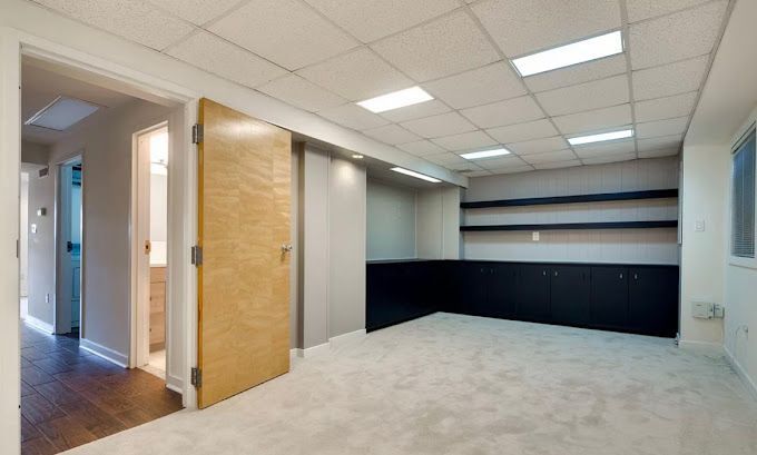 Empty office room with gray carpet, recessed lighting, and built-in shelving and cabinets.