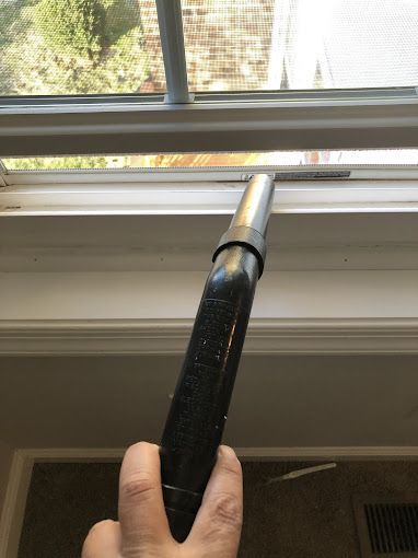 Vacuuming a window sill, close-up with hand holding vacuum wand, view from inside the house.