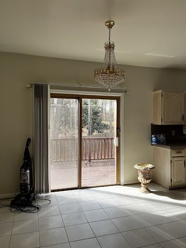 Empty room with sliding door to a deck, chandelier, vacuum cleaner, and kitchen cabinets.