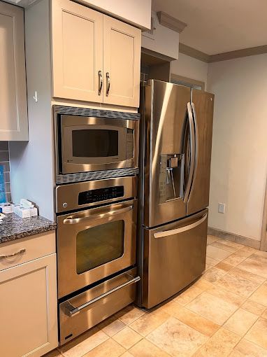 Kitchen with beige cabinets, stainless steel microwave, oven, and refrigerator.