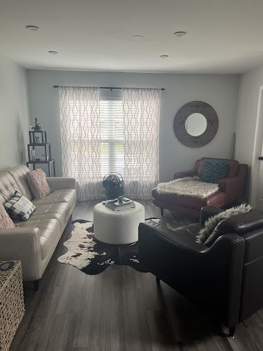 Living room with white sofa, red chaise lounge, and black chair arranged on a cowhide rug.