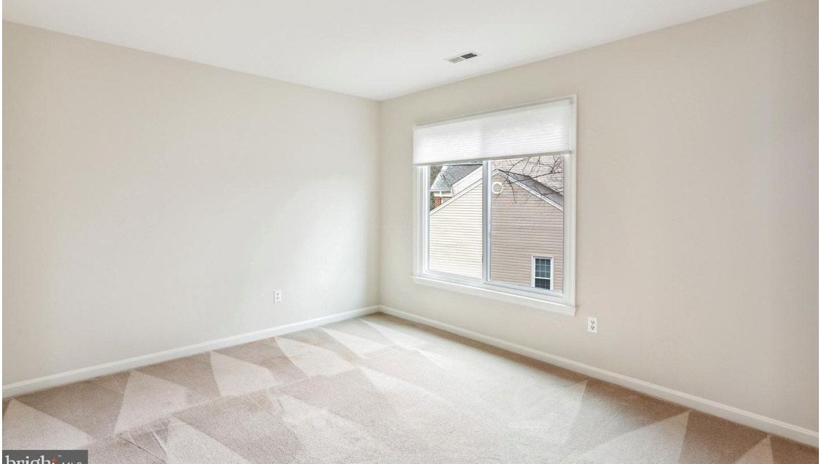 Empty room with beige carpet and walls, window with shade, sunlight.