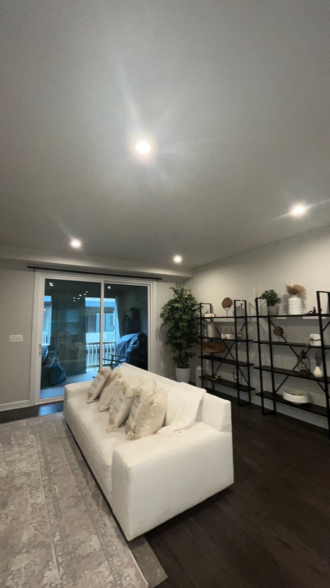 White sofa in modern living room with sliding door to patio and black shelving.