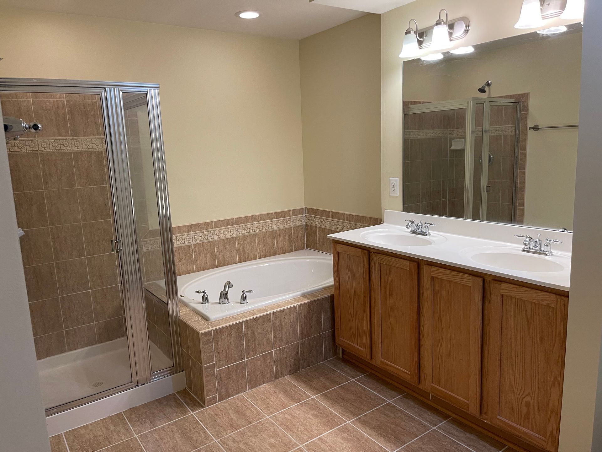 Bathroom with shower, bathtub, vanity, and tan tile.