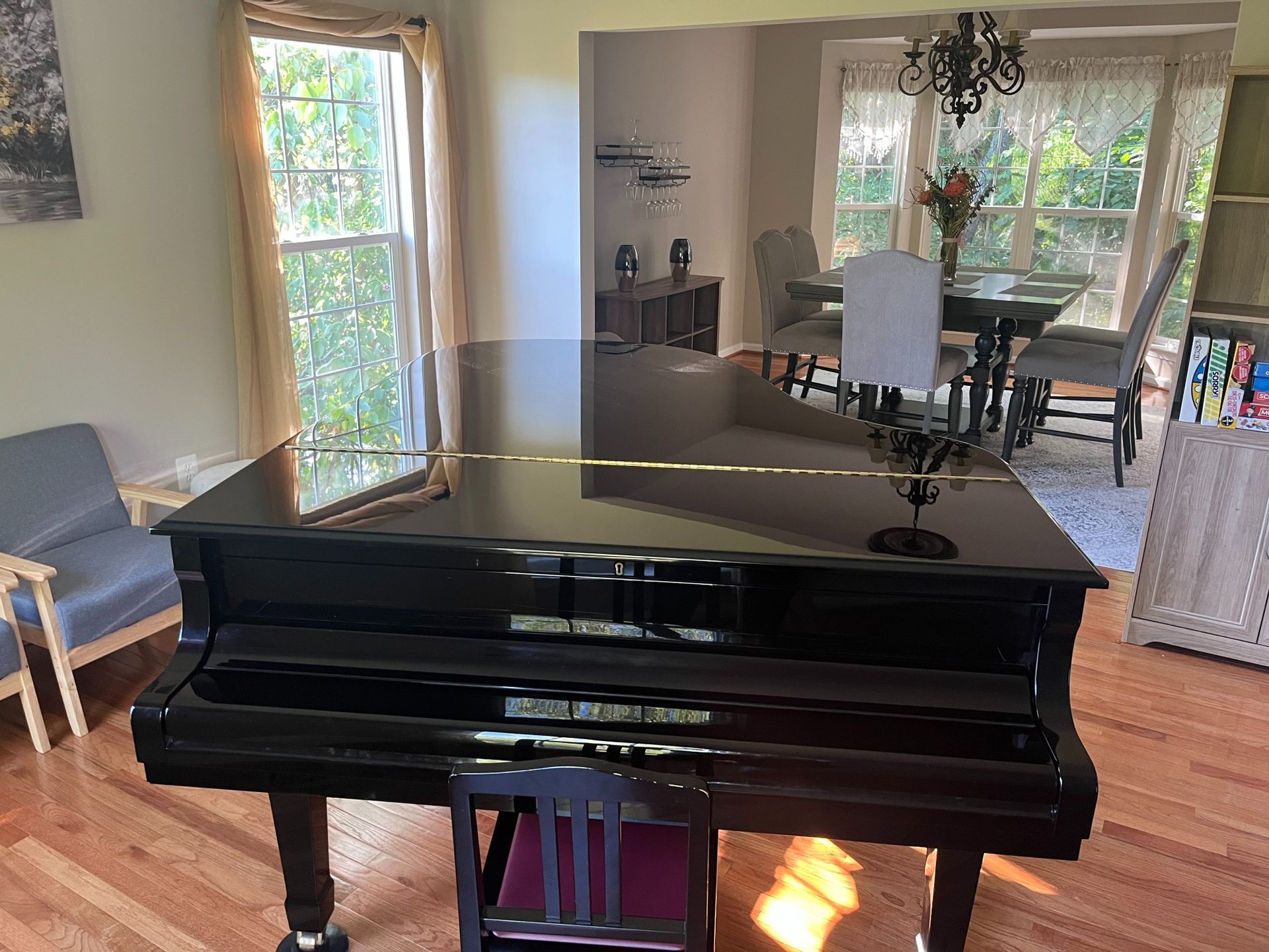 Black grand piano in a room with hardwood floors, a dining area, and a large window.