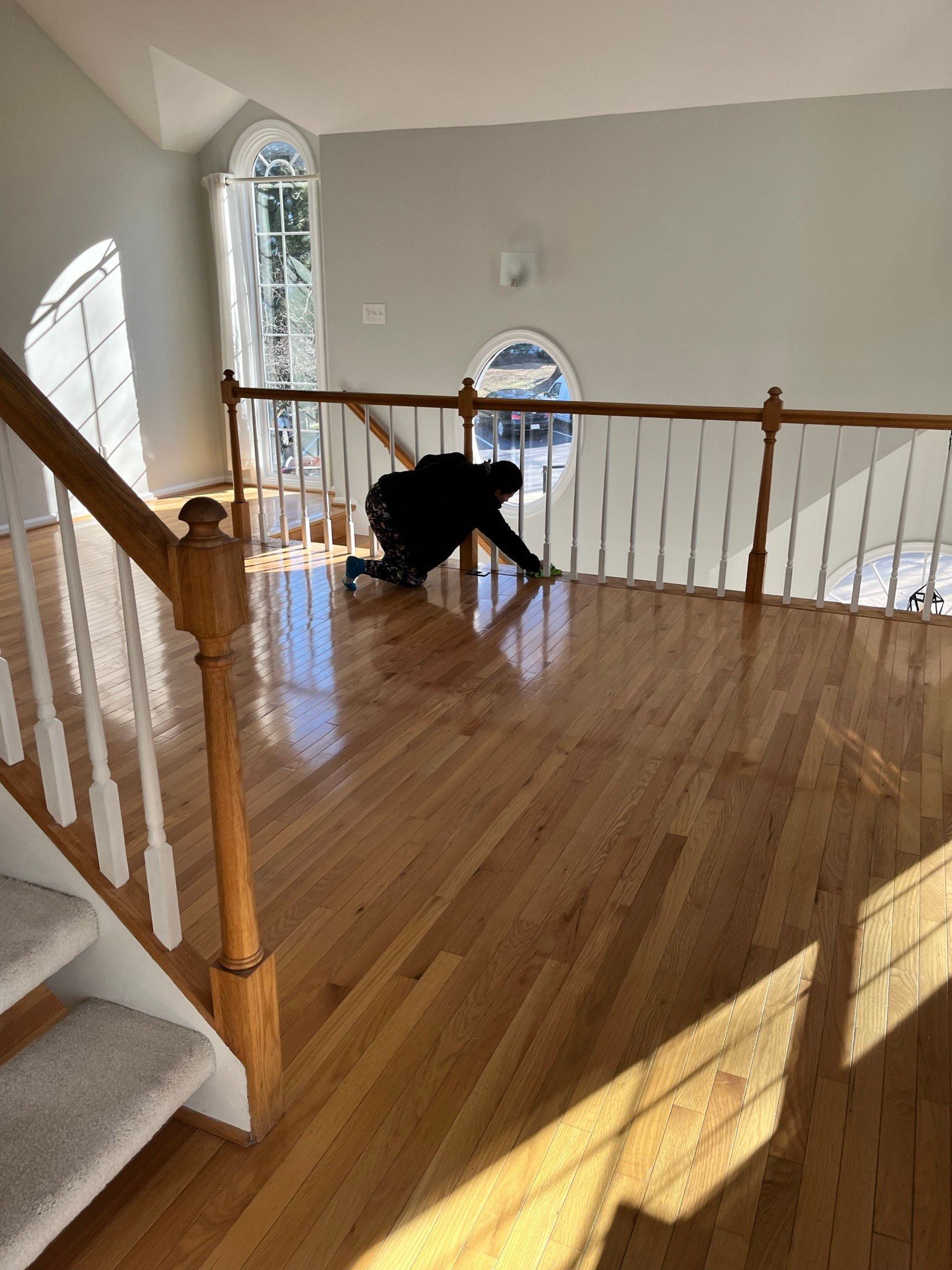 Person on hands and knees examining hardwood floor in a home. Bright sunlight streams through the windows.
