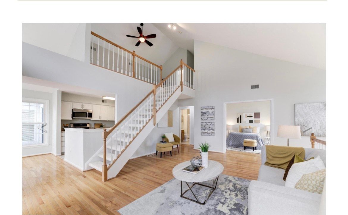 Interior view of a living room with stairs to a loft area, open to a kitchen and bedroom.