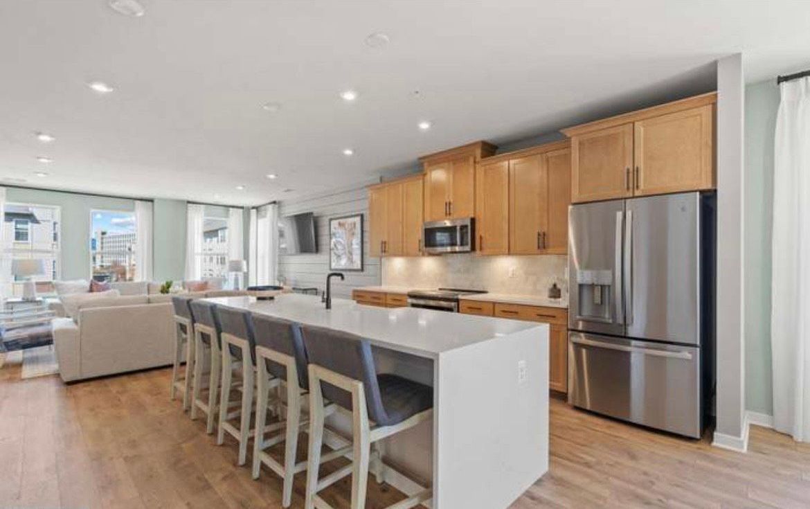 Modern kitchen with light wood cabinets, stainless steel appliances, and a large island with bar stools.