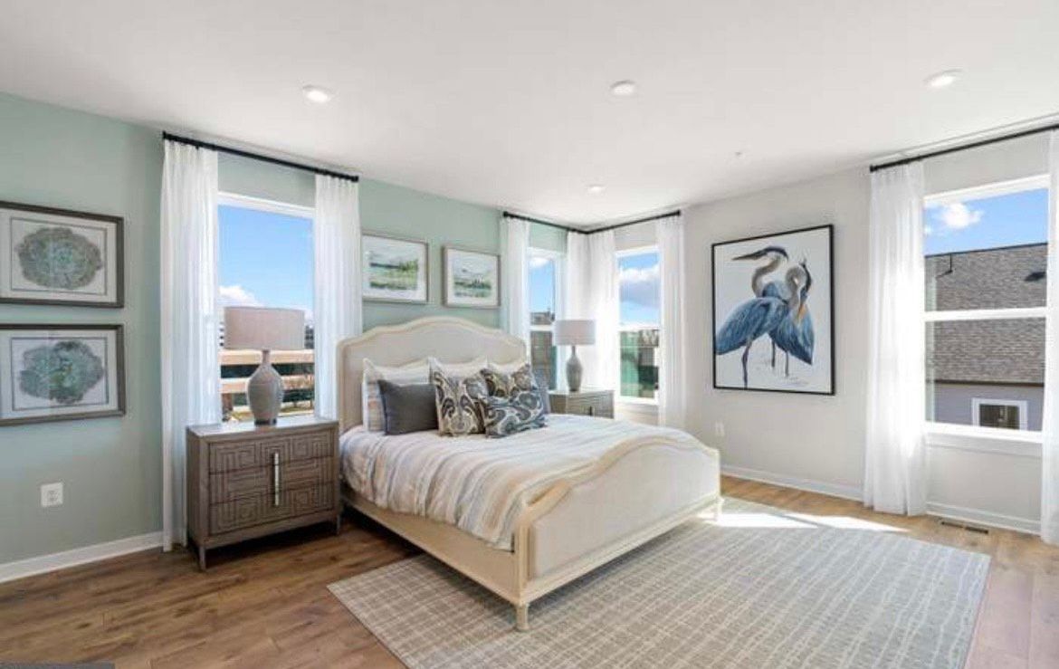 Bedroom with light blue walls, white bed and curtains, wooden nightstand, and rug.