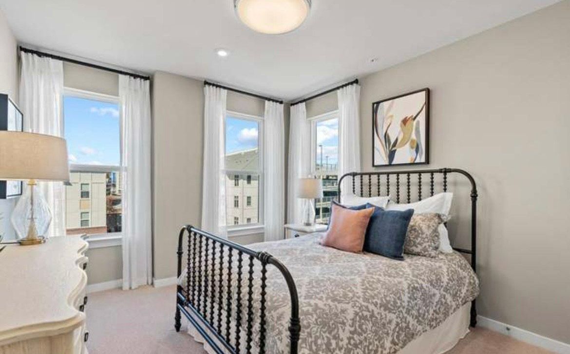 Bedroom with a black metal bed frame, windows with white curtains, and a white dresser.