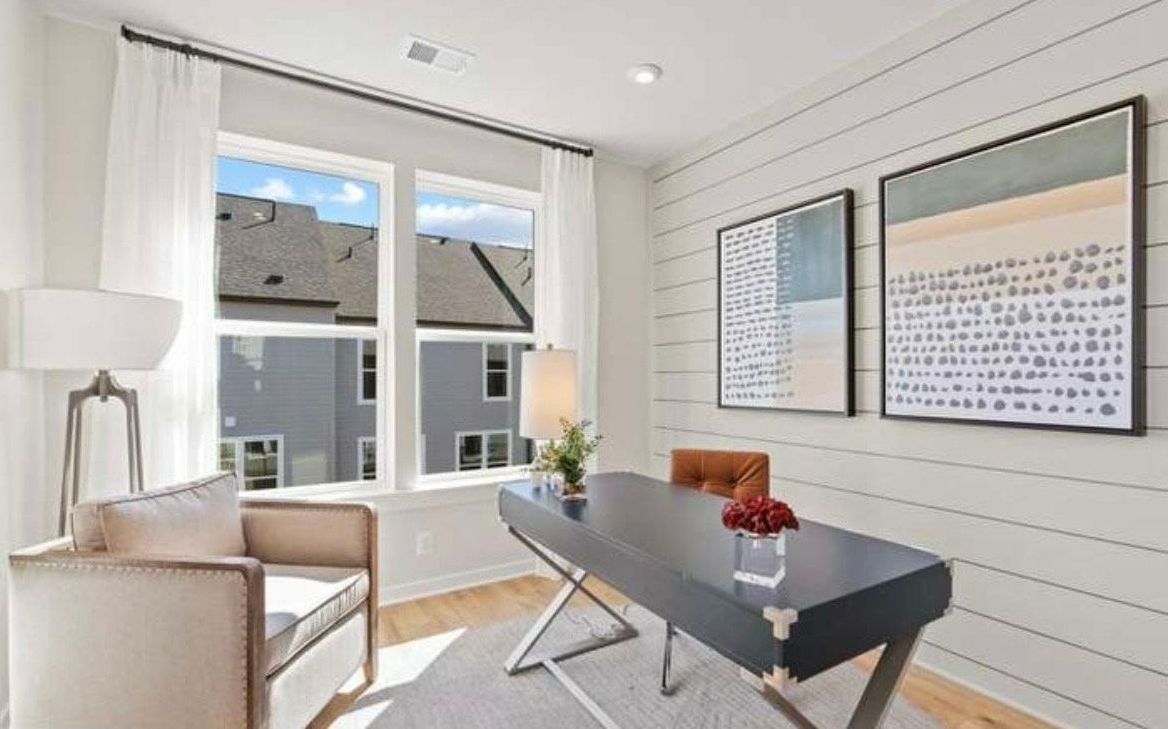 Home office with a desk, chair, and art; large windows look out to the neighborhood.