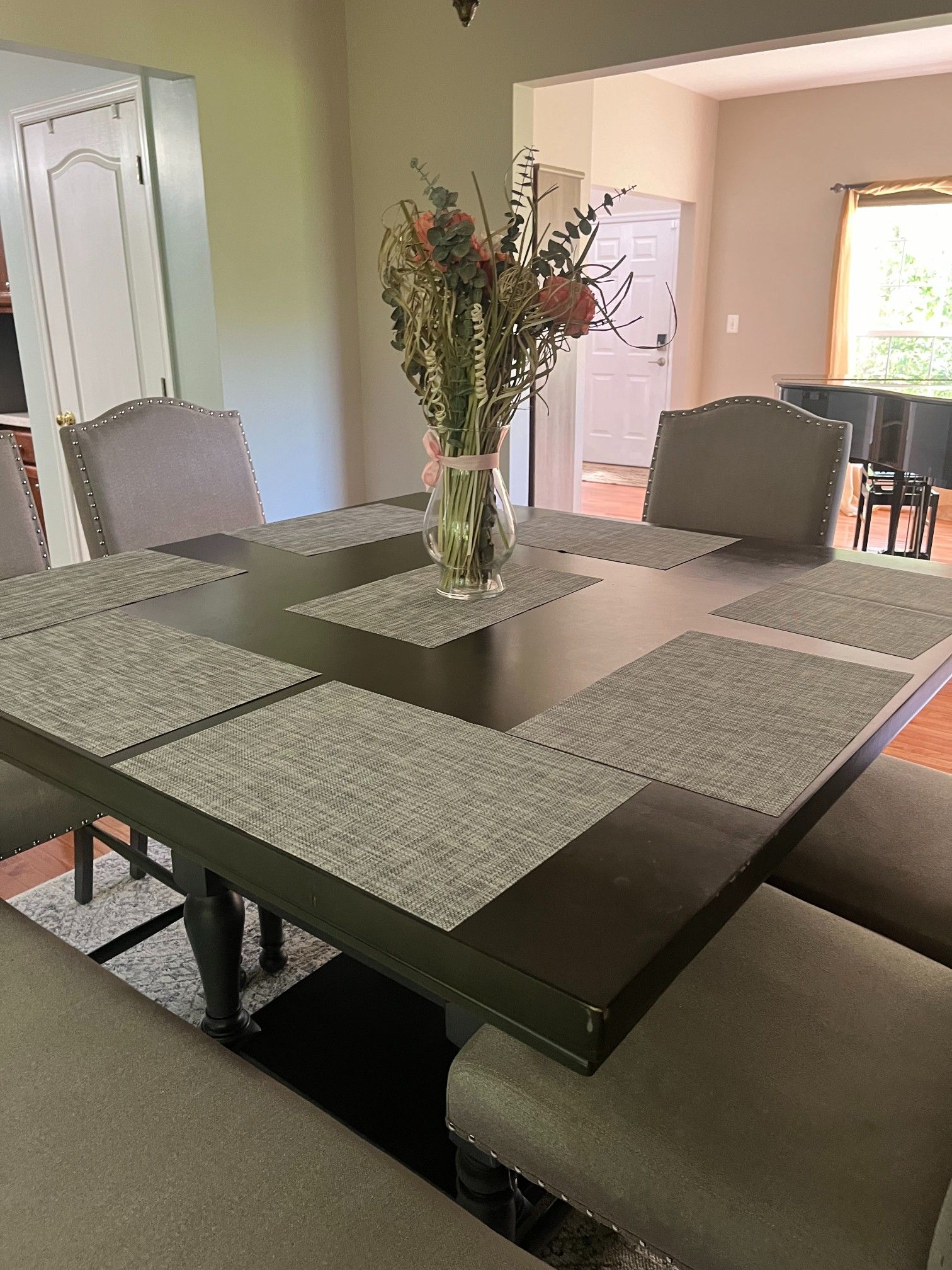 Dining table set with gray placemats, chairs, and a floral centerpiece in a home setting.