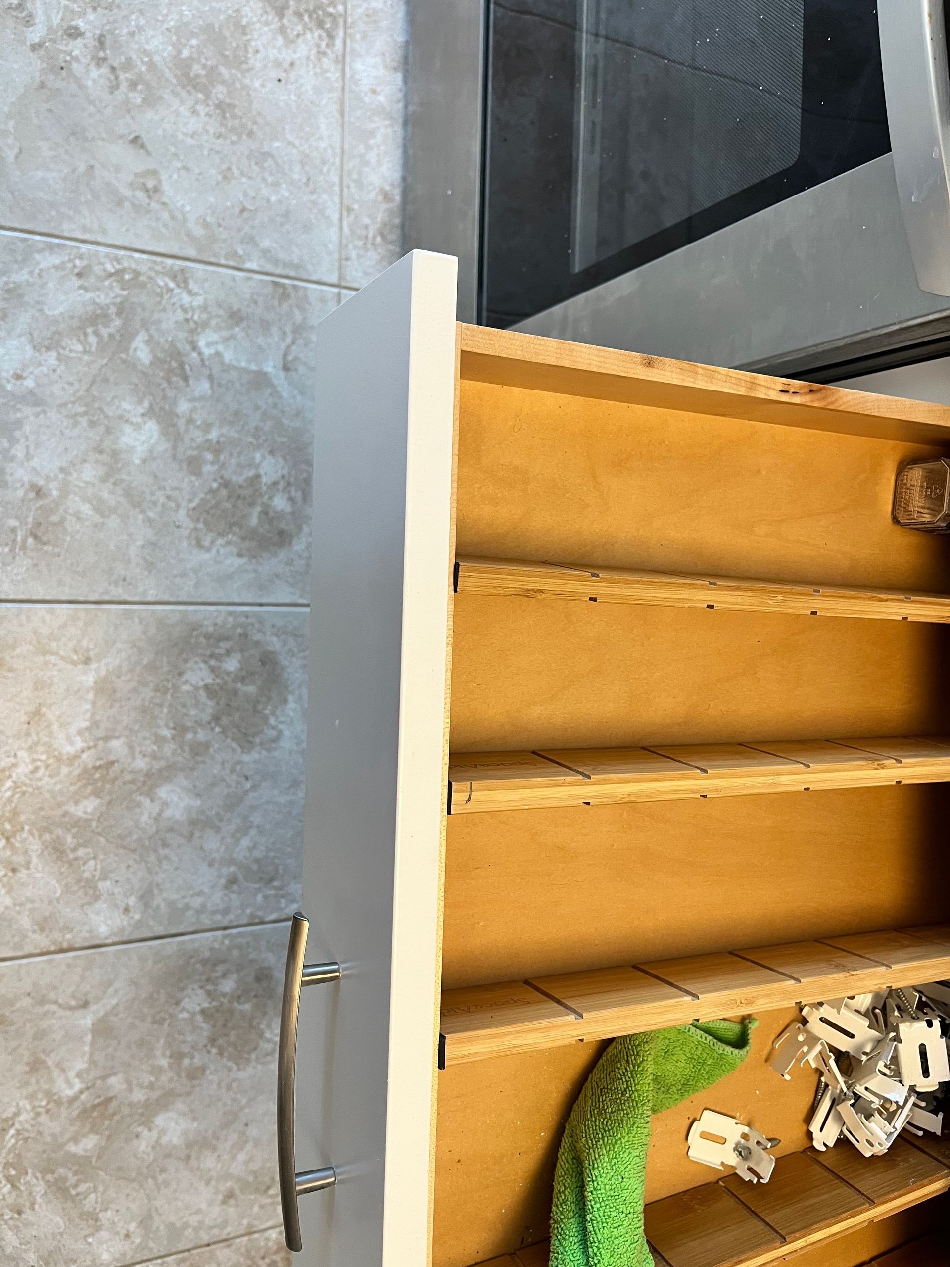 Open white cabinet with wooden shelves; a green cloth and other items are in the bottom.