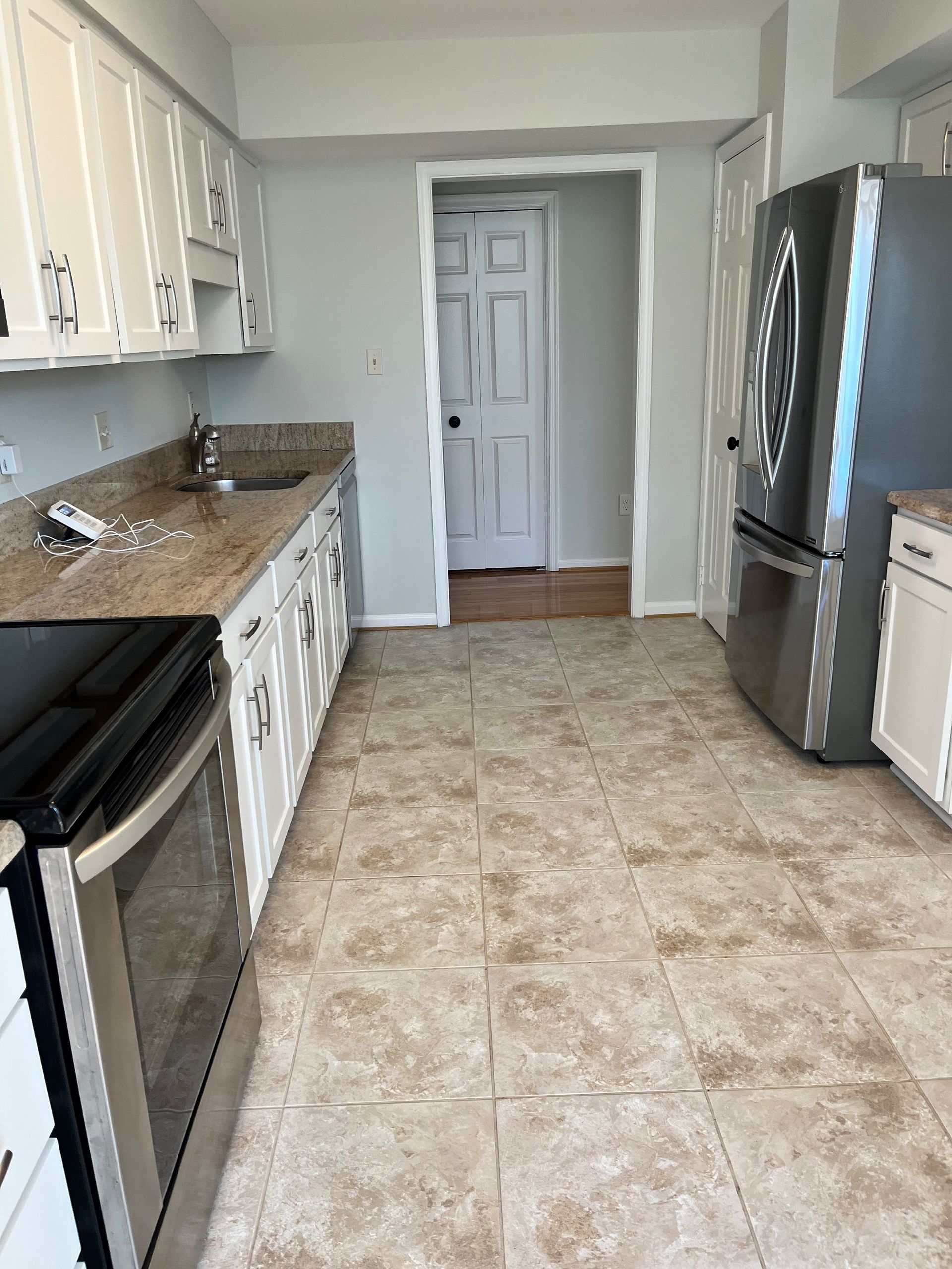 Kitchen with white cabinets, stainless steel appliances, tan countertops and flooring, and a doorway.