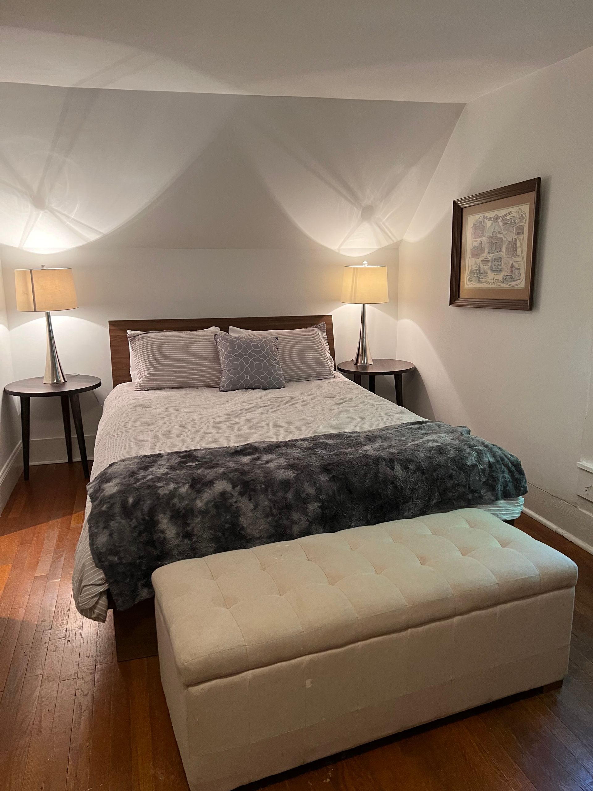 Bedroom with bed, nightstands, lamps, storage bench, and framed art.