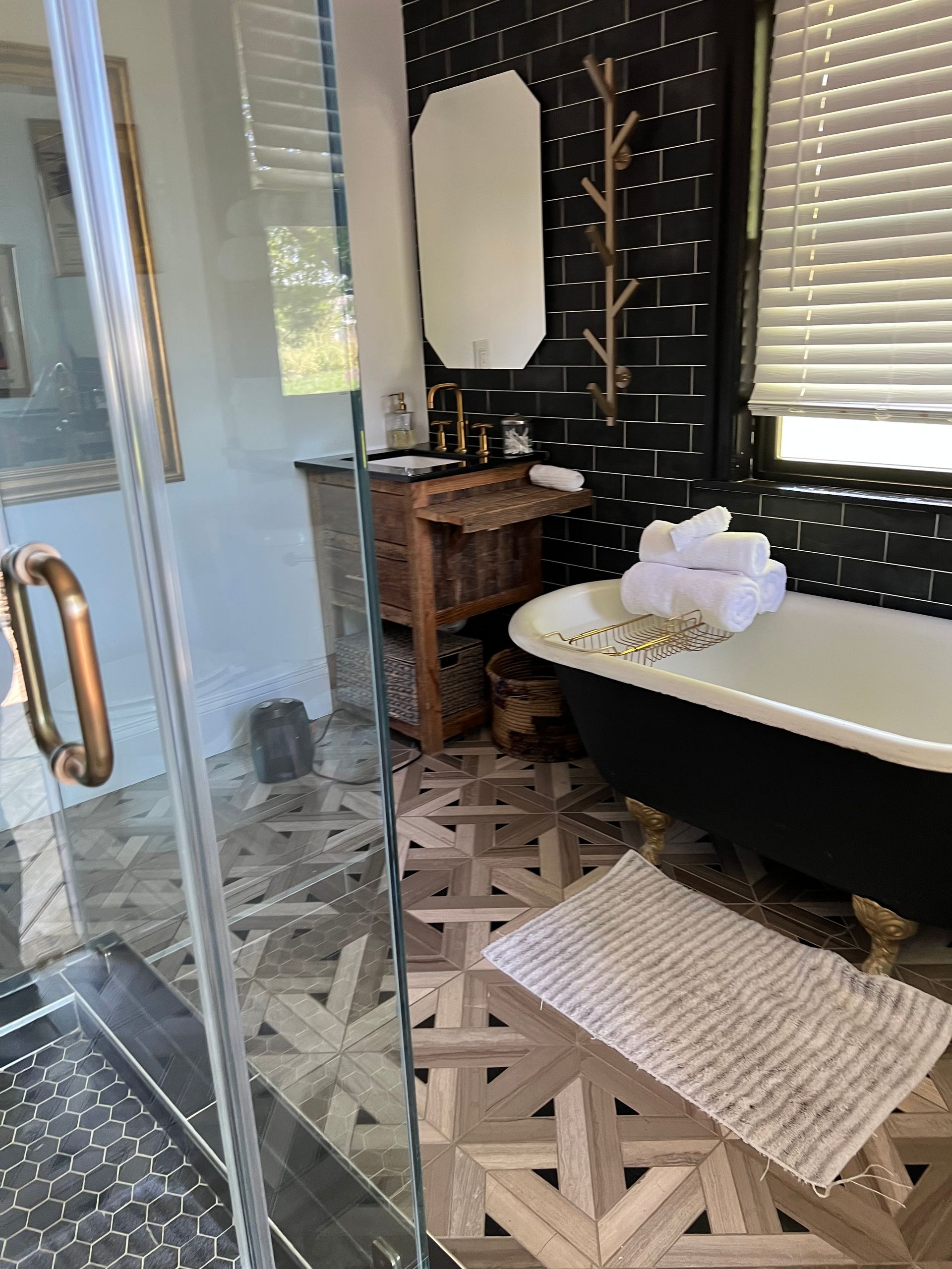 Bathroom with patterned floor, black accent wall, clawfoot tub, and glass shower.