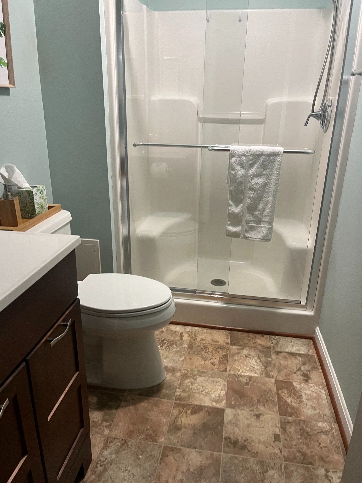 Bathroom with brown tiled floor, toilet, shower with towel, and dark brown vanity.