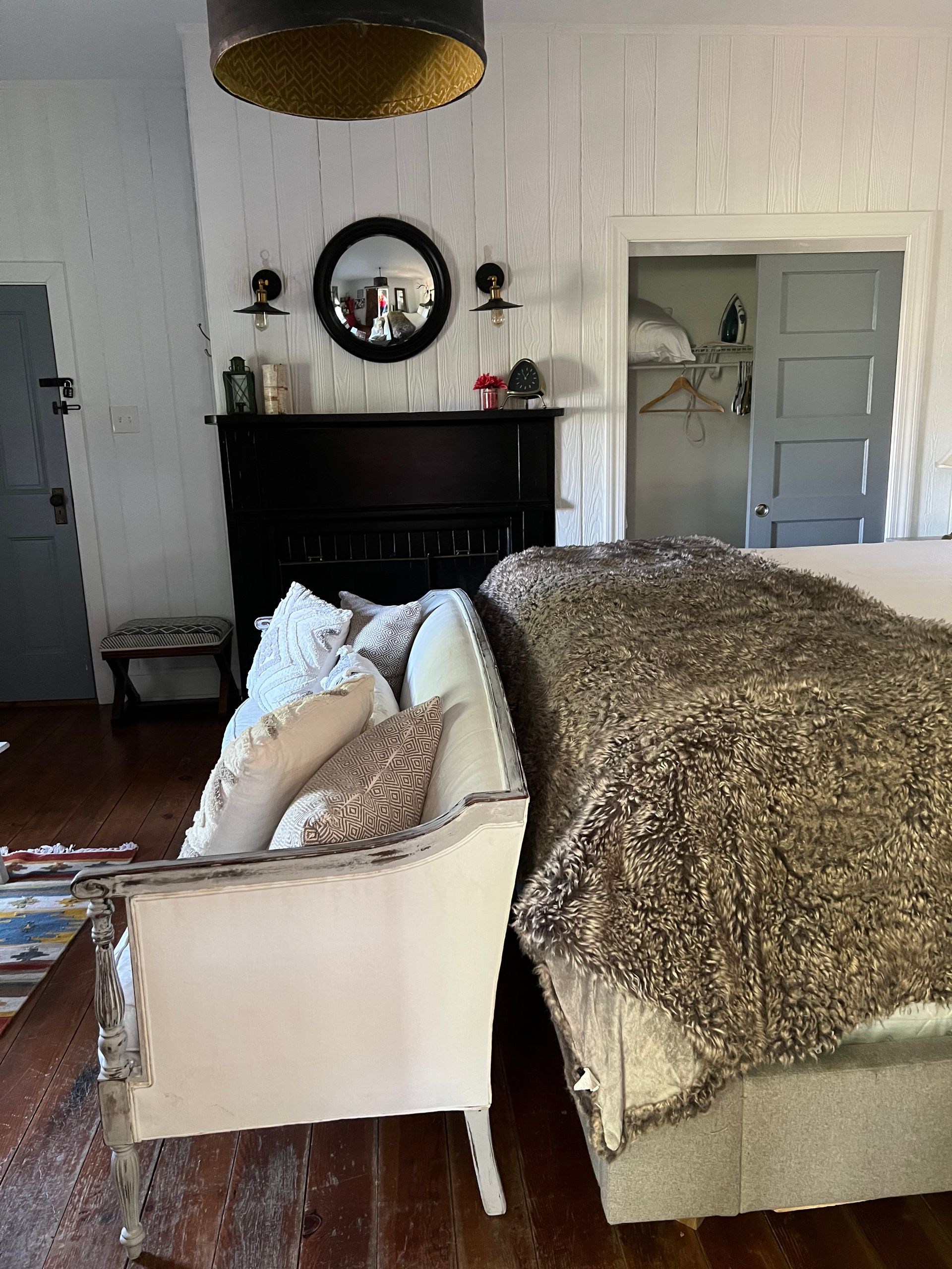 Bedroom interior with couch, bed, fireplace, and closet. Brown, white, and gold tones.