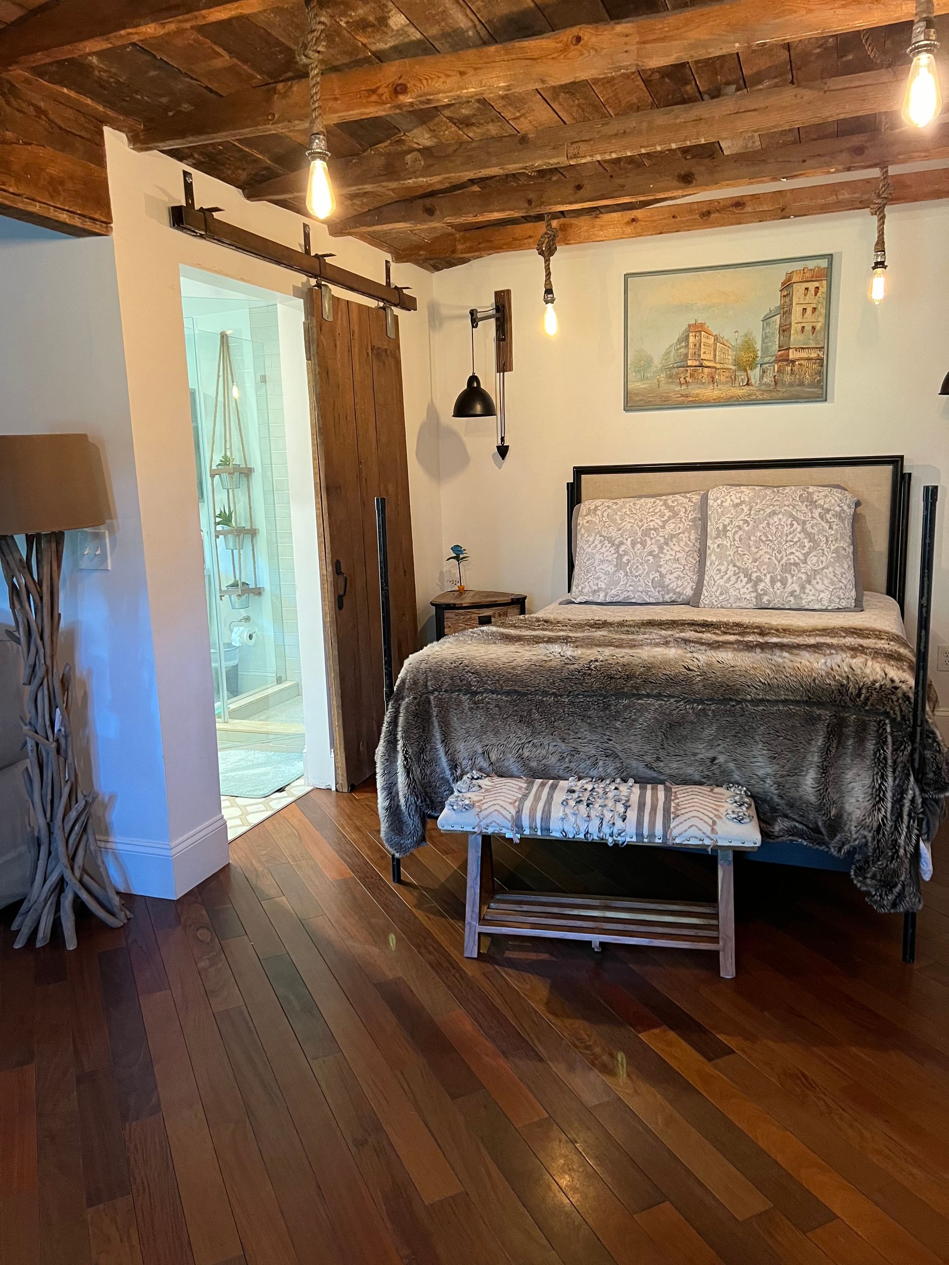 Bedroom with wood floors, exposed beam ceiling, bed with faux fur blanket, and sliding barn door.