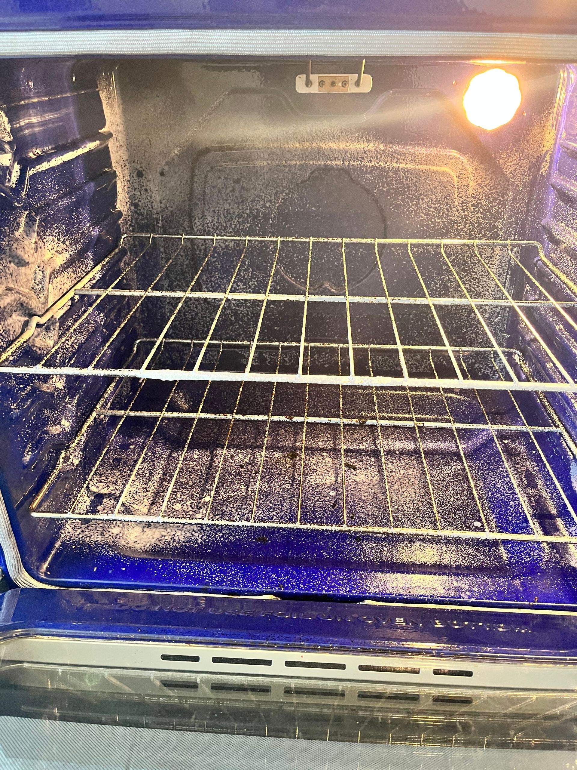Dirty oven interior with white residue coating the walls and rack, light on.