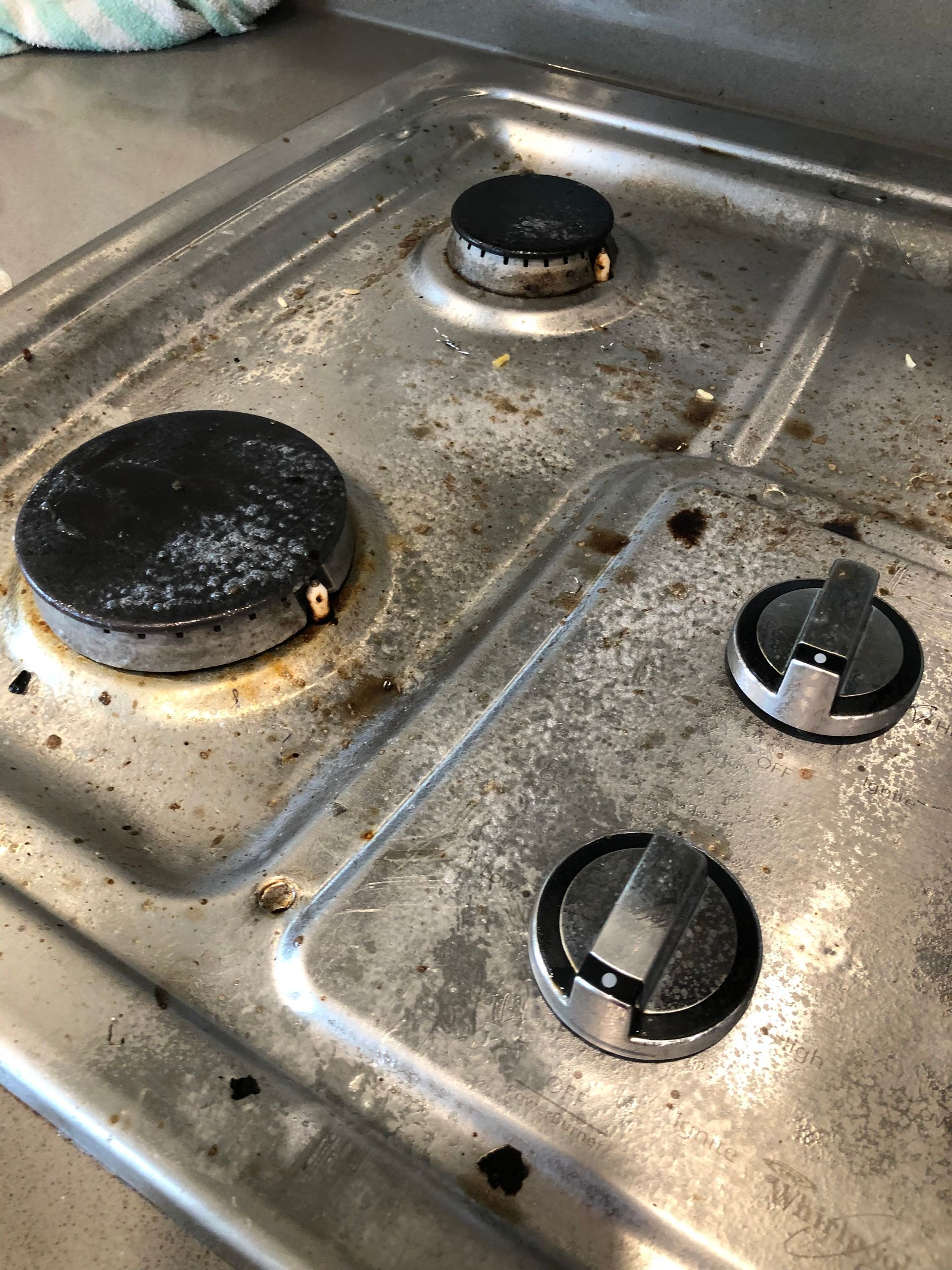 Dirty gas stovetop with three burner grates and control knobs.