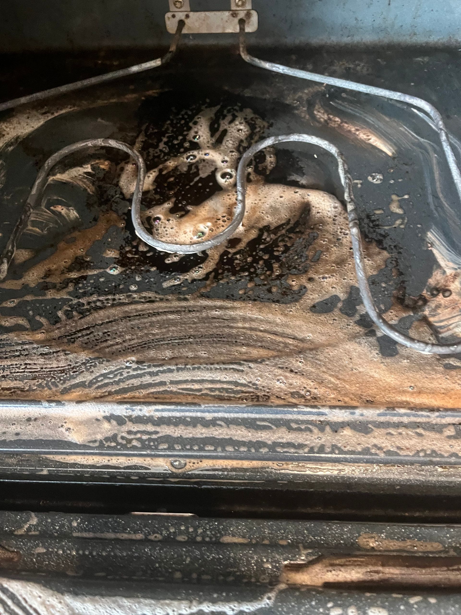 Dirty oven interior, burnt food and cleaning foam visible on the surface.