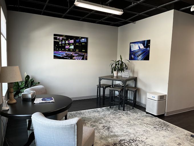 Awaiting area with round table, armchairs, small table, stools, rug, and TV control panel display.