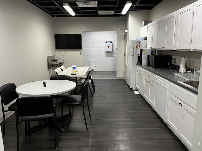 Office break room with tables, chairs, cabinets, appliances, and a mounted TV.