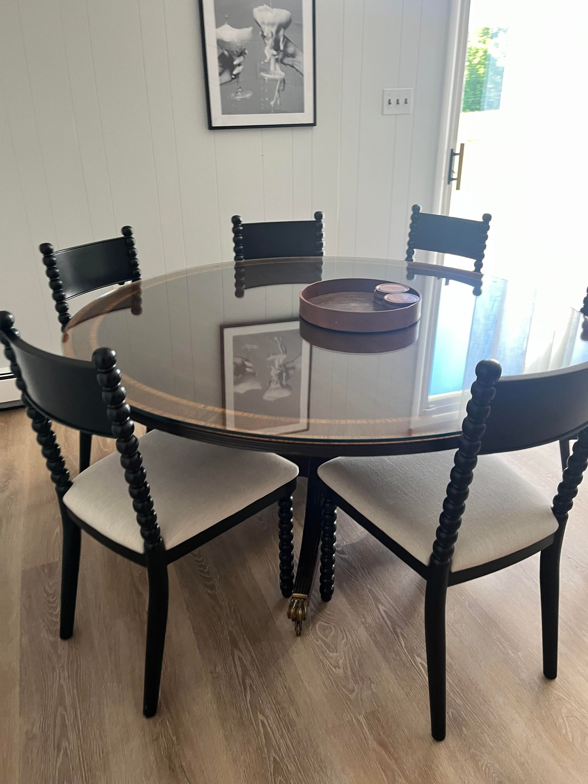 Round black dining table with six black spindle-back chairs; room with art on wall, and glass door.