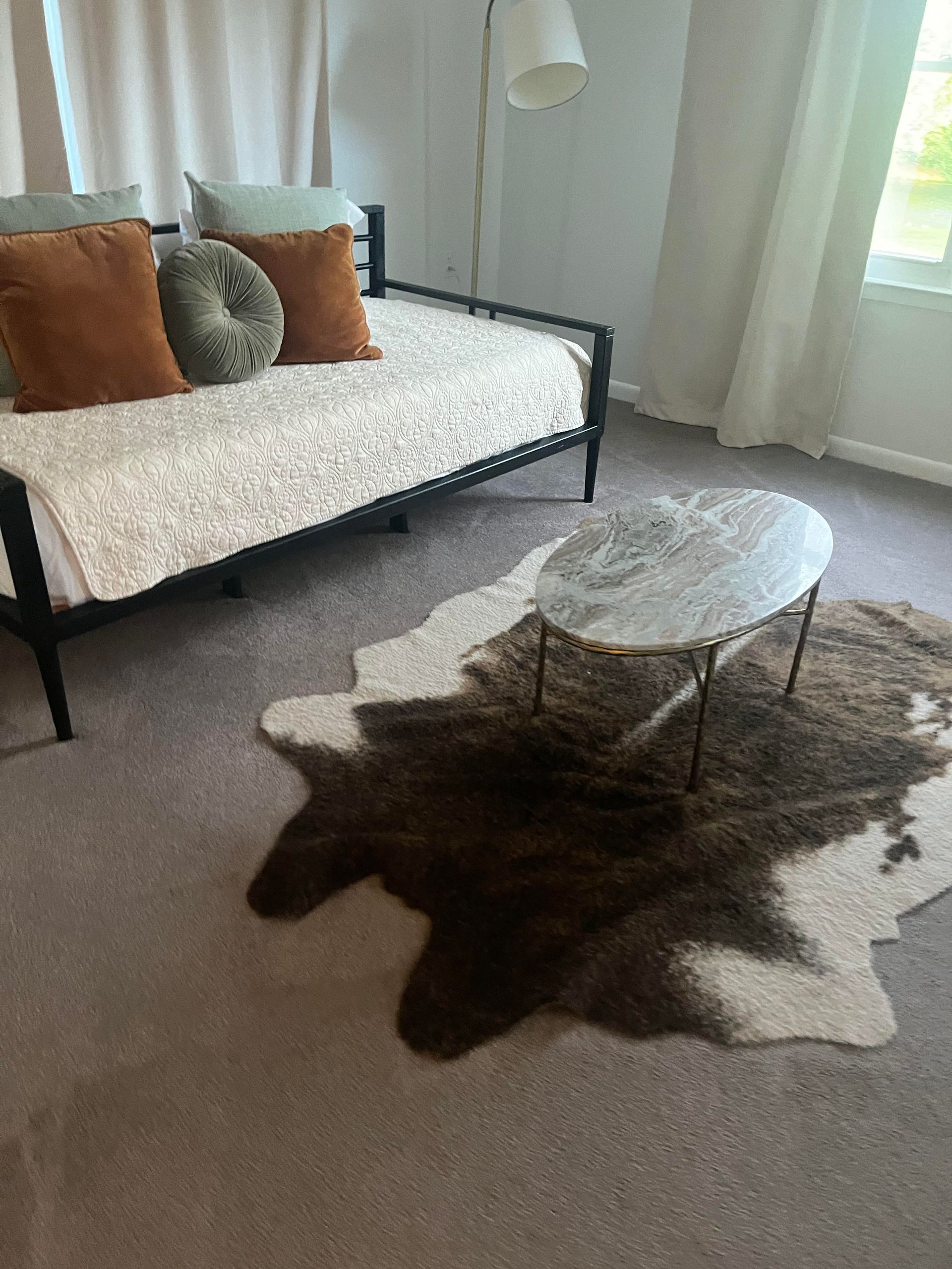 Room with a daybed, cowhide rug, and marble-topped coffee table.  Brown, tan, and white color palette.
