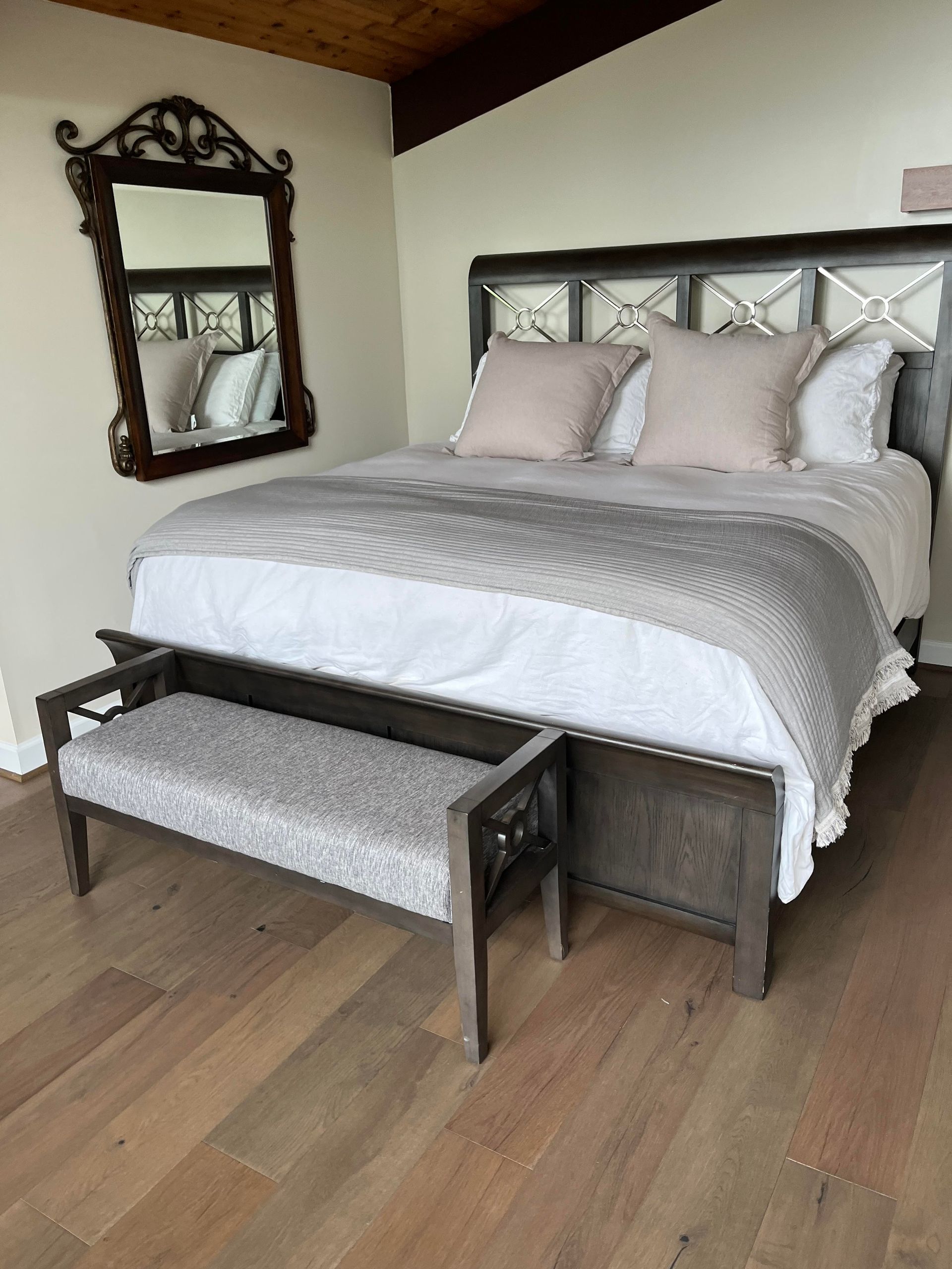 Bedroom with bed, bench, and mirror; gray, beige, brown tones; wooden floors.