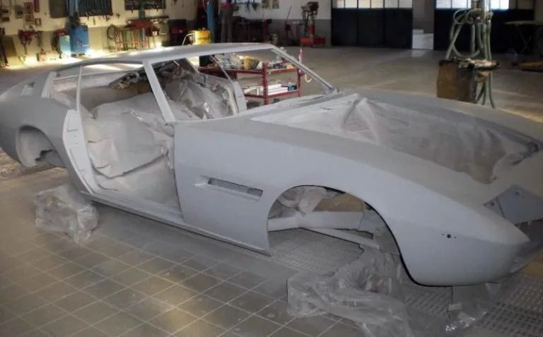 Carrozzeria grigia in un'officina, con le portiere aperte, ricoperta di plastica protettiva.
