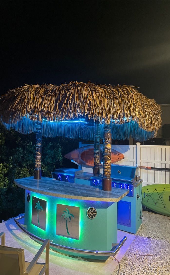 A tiki bar with a thatched roof is lit up at night.