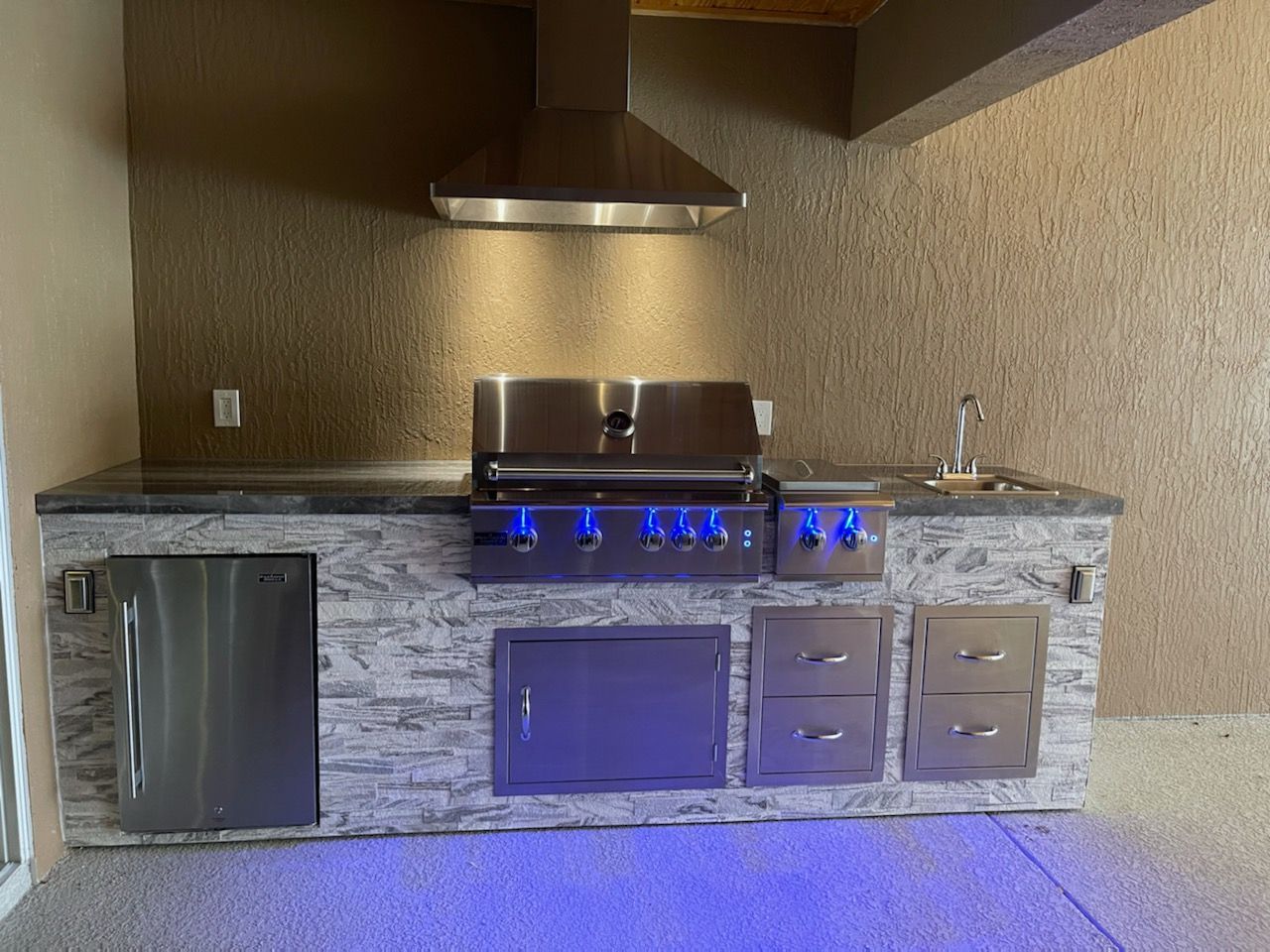 A stainless steel grill is sitting on top of a stone counter in a kitchen.