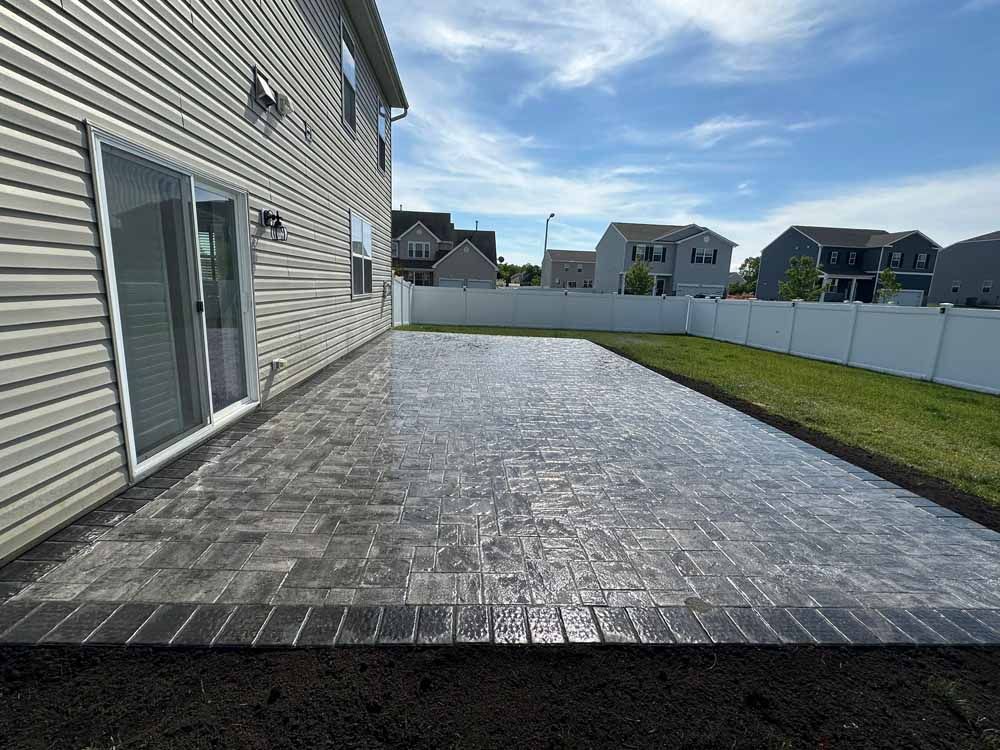 The backyard of a house with a patio and a white fence.