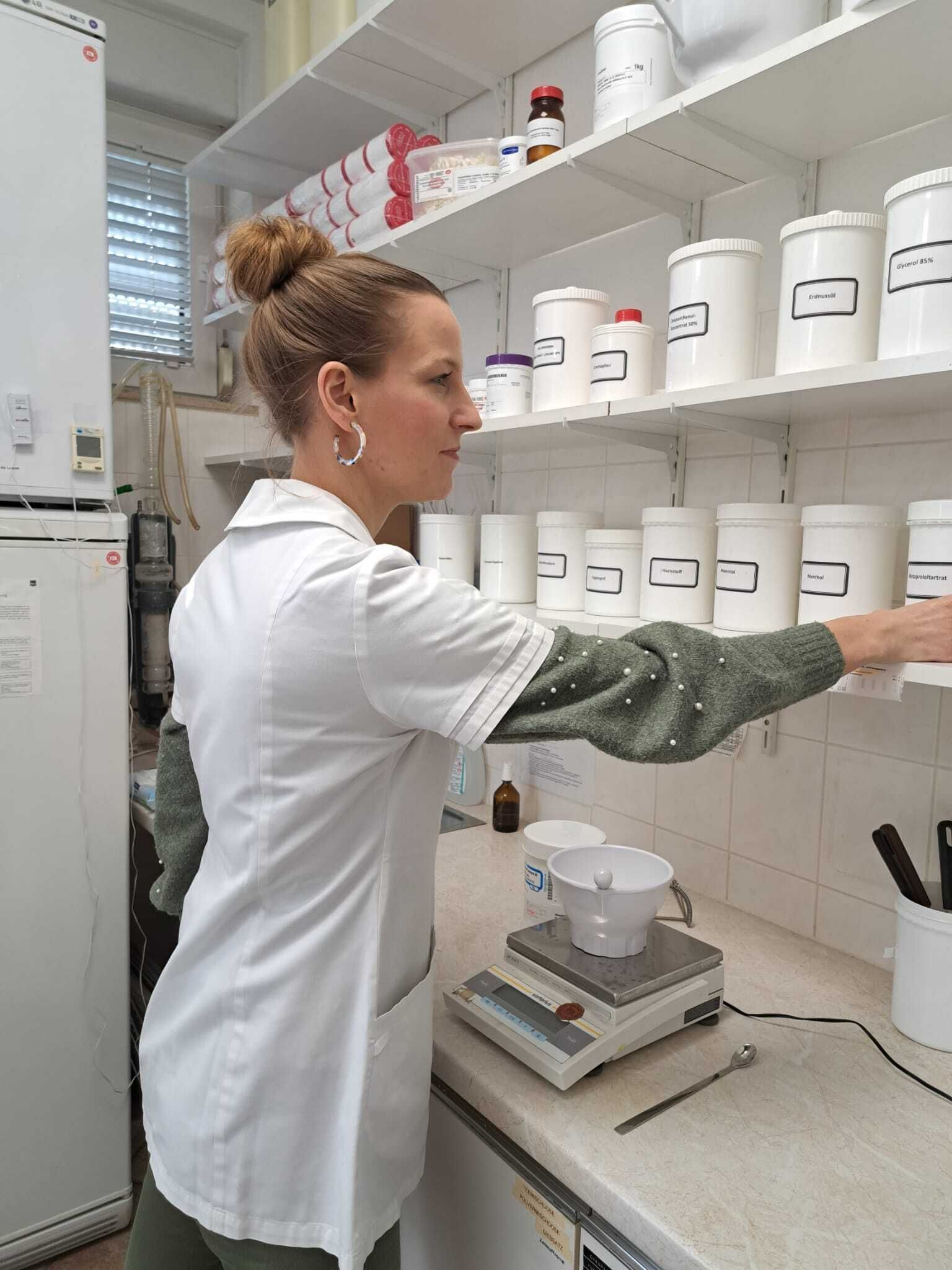 Eine Frau im Laborkittel arbeitet in einer Apotheke.