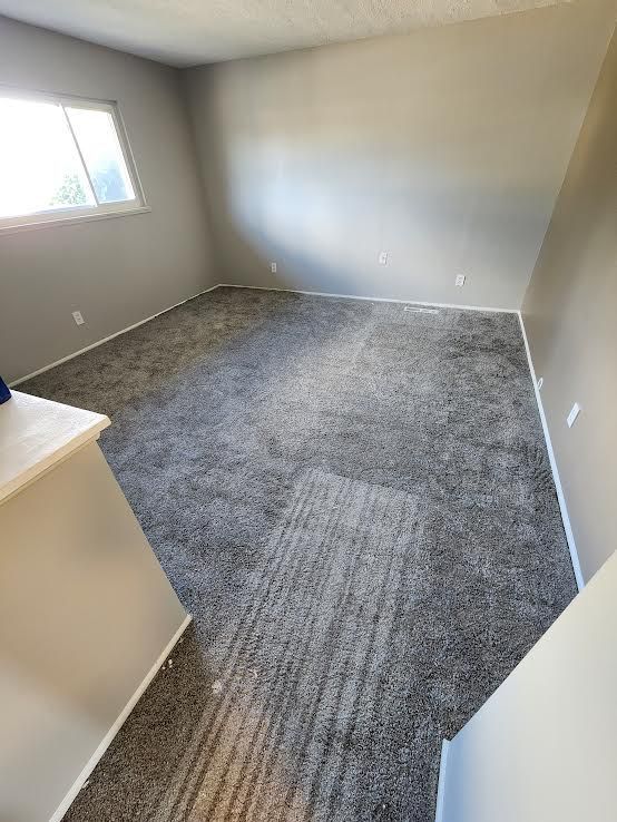 Empty room with gray walls and carpet. A small window is on the left.
