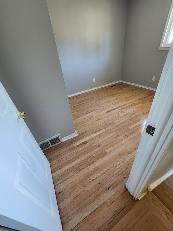 Empty room with hardwood floors, gray walls, and white door.