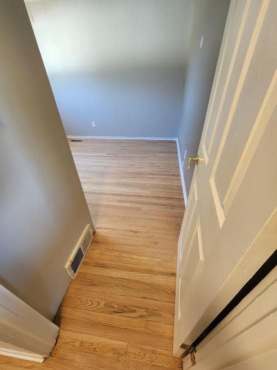 View from a doorway into a room with hardwood floors and gray walls. A white door is on the right.